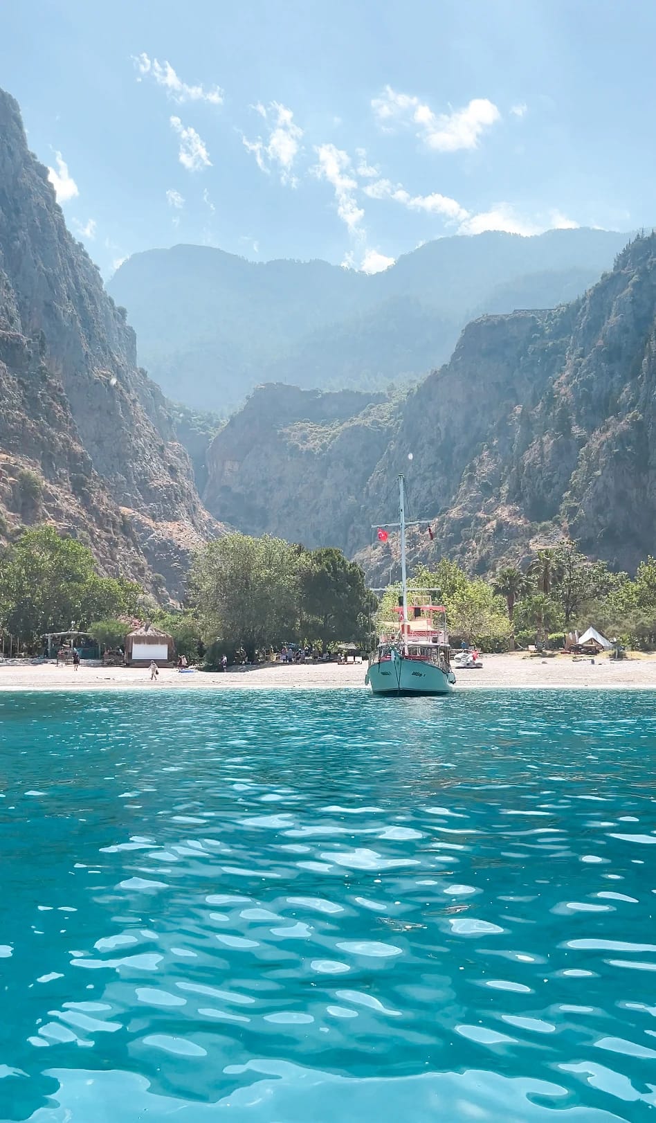 Blick vom türkisfarbenen Wasser auf den Strand von Butterfly Valley zwischen steilen Felswänden.