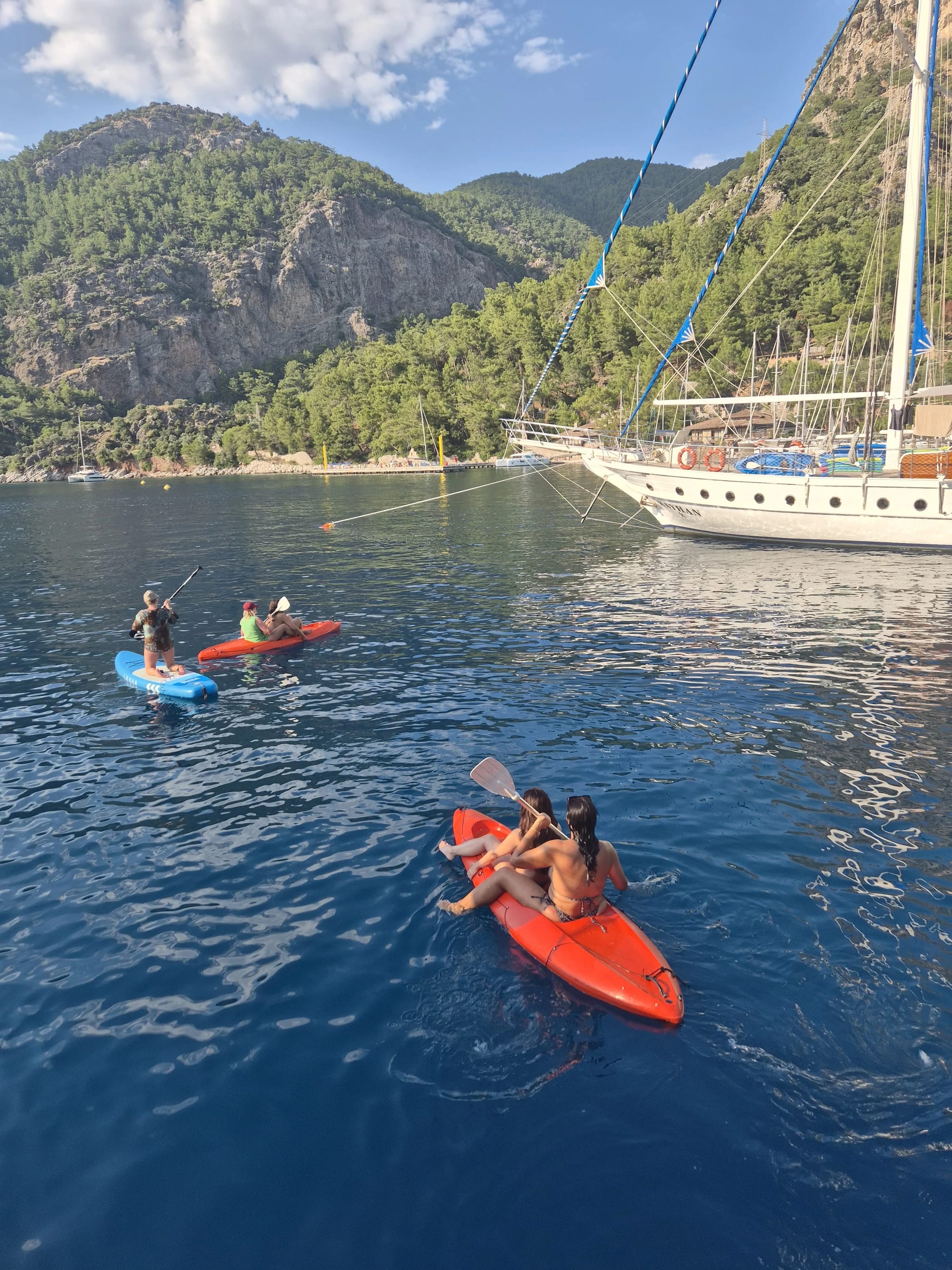 Zwei Frauen paddeln im Kajak vor einem Segelboot in der Bucht von Fethiye.